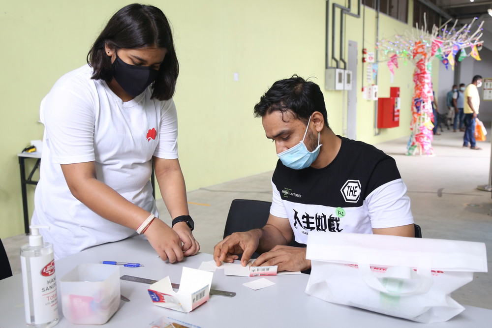 Tzu Ching youth volunteer Anushri Bhattacharya helping a migrant worker with the making of the mask holder. (Photo by Alice Toh)